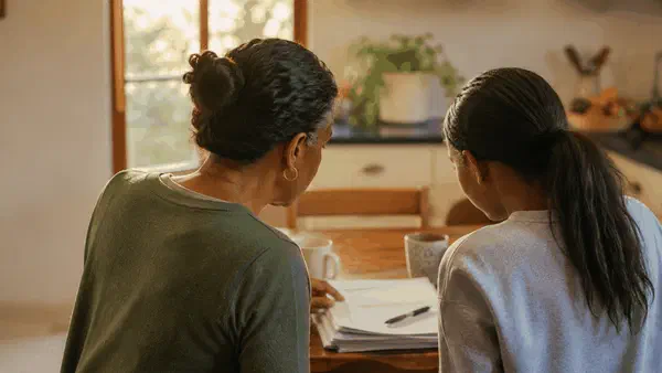 Parent and teenager looking through school reports together at a kitchen table